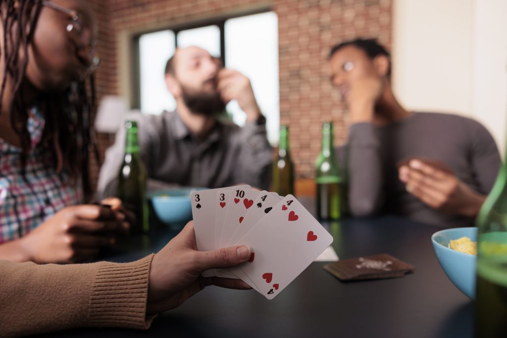 Close up shot of woman hand holding card games while enjoying fun leisure activity with best friends. Person playing card games with people having snacks and beverages while sitting at home.